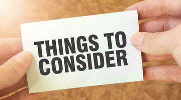 THINGS TO CONSIDER word inscription on white card paper sheet in hands of a businessman. photo