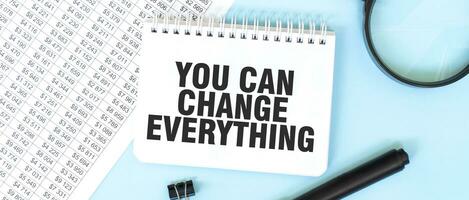 White notepad and magnifier on the financial documentation. Text YOU CAN CHANGE EVERYTHING. Business concept photo
