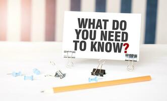 WHAT DO YOU NEED TO KNOW sign on paper on white desk with office tools. Blue and white background photo