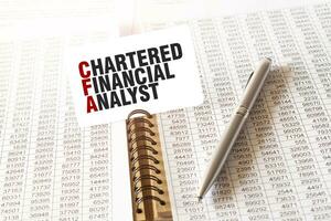 Text CHARTERED FINANCIAL ANALYST on paper card, pen, financial documentation on table photo