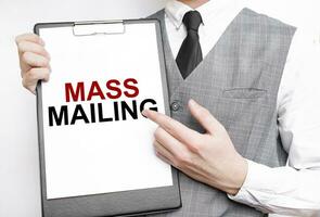 MASS MAILING inscription on a notebook in the hands of a businessman on a gray background, a man points with a finger to the text photo