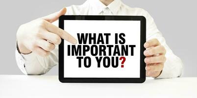 Text WHAT IS IMPORTANT TO YOU on tablet display in businessman hands on the white background. Business concept photo