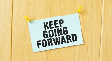 KEEP GOING FORWARD sign written on sticky note pinned on wooden wall photo