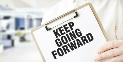 Text KEEP GOING FORWARD on white paper plate in businessman hands in office. Business concept photo