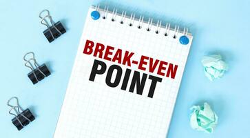 White notepad with text BREAK-EVEN POINT and office tools on the blue background photo