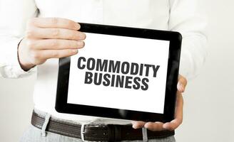 Text COMMODITY BUSINESS on tablet display in businessman hands on the white background. Business concept photo