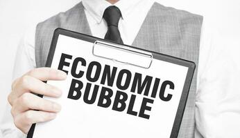 ECONOMIC BUBBLE inscription on a notebook in the hands of a businessman on a gray background, a man points with a finger to the text photo