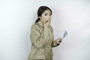 A shocked young government worker woman is wearing khaki uniform holding cash money in Indonesian rupiah isolated by white background photo