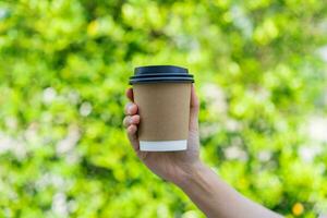 Young male hand holding a coffee paper cup isolated on green nature background photo