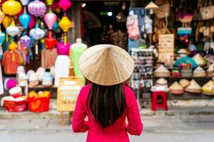 Young female tourist in Vietnamese traditional dress looking at a souvenir shop in Hoi An Ancient town photo