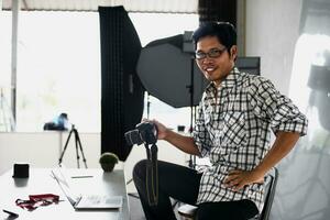 Happy young photographer holding dslr camera in her home office Female photographer smiling cheerfully while working at table Creative man working on new project. photo