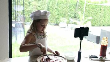 Girl of 6 years old is preparing pizza with tomatoes sauce and violet onion in front of her subscribers. video