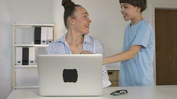 a boy giving a flower to the working mother sitting at a desk with a laptop video