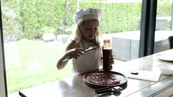 ragazza di 6 anni vecchio è preparazione Pizza con pomodori salsa e viola cipolla nel davanti di sua iscritti. video