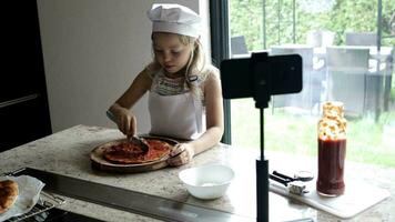 flicka av 6 år gammal är framställning pizza med tomater sås och violett lök i främre av henne abonnenter. video