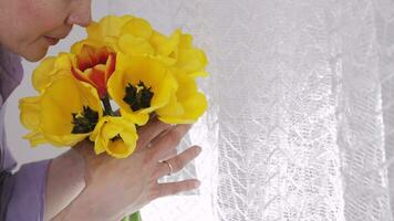 een vrouw ruiken geel tulpen van achter een gordijn video