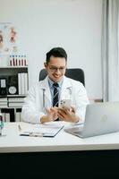 Physician doctor sit on table in hospital. Attractive therapist male practitioner pharmacist smile and use tablet and laptop. after success work from treatment photo