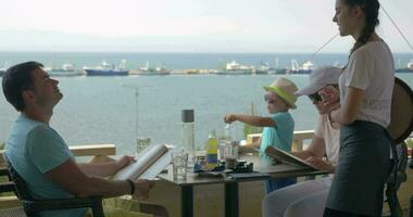 en el mar costa de ciudad perea, Grecia un joven familia se sienta en café video