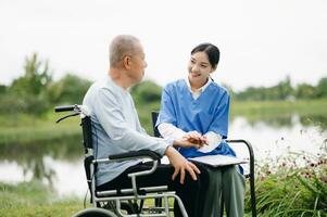 Elderly asian senior man on wheelchair with Asian careful caregiver. Nursing home hospital garden concept. photo