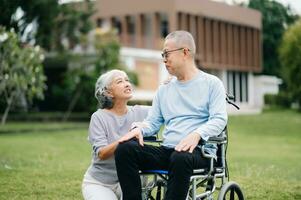 Asian Senior couple sitting in wheelchairs taking care of each other.in romantic time They laughing and smiling while sitting outdoor in park. photo