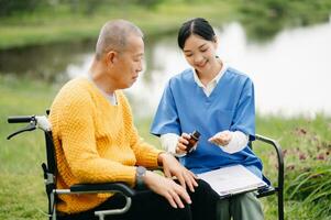 Elderly asian senior man on wheelchair with Asian careful caregiver. Nursing home hospital garden concept. photo