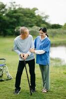 Elderly asian senior man on wheelchair with Asian careful caregiver. Nursing home hospital garden concept. photo