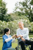 Elderly asian senior man on wheelchair with Asian careful caregiver and encourage patient, walking in garden. with care from a caregiver and senior health insurance. photo