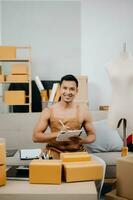 Startup small business SME, Entrepreneur owner man using smartphone or tablet taking receive and checking online purchase shopping order to preparing pack product box. photo