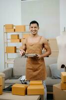 Startup small business SME, Entrepreneur owner man using smartphone or tablet taking receive and checking online purchase shopping order to preparing pack product box. photo