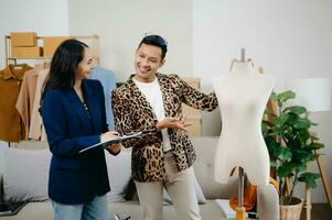 Couple of fashion designers working with fabric and clothing sketches at the studio full of tailoring tools and holds tablet and laptop. photo