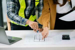 Two colleagues discussing data working and tablet, laptop with on architectural project at construction site at desk in modern office photo