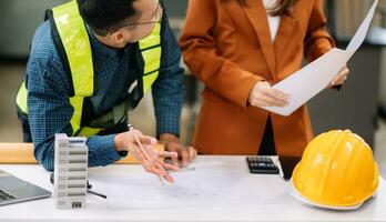 Two colleagues discussing data working and tablet, laptop with on architectural project at construction site at desk in modern office photo