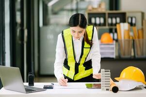 Creative architect projecting on the big drawings working and laptop with on on architectural project at construction at desk in office. Asian woman industry professional photo