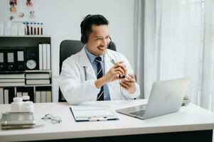 Attractive male doctor talking while explaining medical treatment to patient through a video call with laptop in office photo