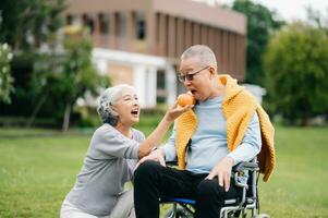 Asian Senior couple sitting in wheelchairs taking care of each other.in romantic time They laughing and smiling while sitting outdoor in park. photo
