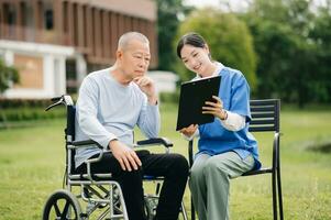 Elderly asian senior man on wheelchair with Asian careful caregiver. Nursing home hospital garden concept. photo