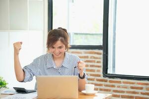 Beautiful young teen Asian business woman using computer laptop with hands up in winner is a gesture, Happy to be successfully celebrating achievement success. photo