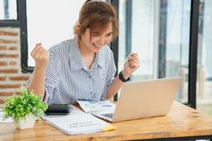 Beautiful young teen Asian business woman using computer laptop with hands up in winner is a gesture, Happy to be successfully celebrating achievement success. photo