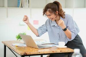 Beautiful young teen Asian business woman using computer laptop with hands up in winner is a gesture, Happy to be successfully celebrating achievement success. photo