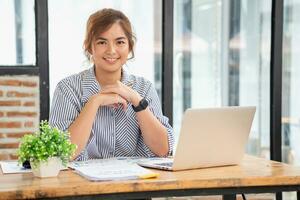 Asian businesswoman calculating company sales with calculator, laptop, and tablet on table Interior of businesswoman office at the modern workstation. photo