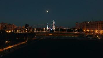 antenne nacht visie van verlicht ferris wiel en brug tegen lucht met maan , valencia, Spanje video