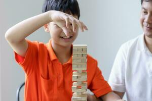 Asian father and son playing wood blocks game Carefree kid playing wood blocks game building constructor from blocks with father at home photo