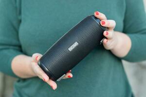 Young girl holds Nomi black portable USB speaker by Nomi electronics company. New Outstanding Mobile Ideas photo