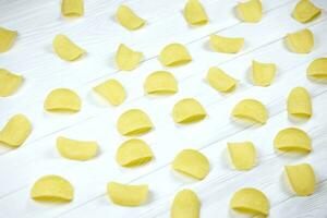 Many orange Pringles potato snack chips on white wooden table. Pringles is a brand of potato snack chips owned by Kellogg Company photo