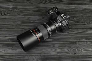 Canon EOS R photocamera and mount adapter EF - EOS R with Canon 105mm f2.8 lens on black wooden table. Photography equipment by Canon inc. photo
