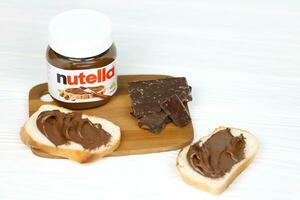 kharkov, ucrania - 27 de diciembre de 2020 lata de vidrio de nutella y untada en pan recién horneado. nutella es fabricada por la empresa italiana ferrero introducida por primera vez en 1964 foto