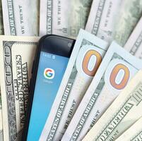 Smartphone screen with Google app and lot of hundred dollar bills. Business and social networking concept photo