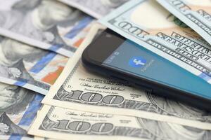 Smartphone screen with Facebook app and lot of hundred dollar bills. Business and social networking concept photo