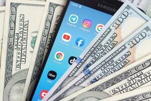 Smartphone screen with many popular apps and lot of hundred dollar bills. Business and social networking concept photo