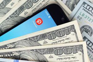 Smartphone screen with Pinterest app and lot of hundred dollar bills. Business and social networking concept photo